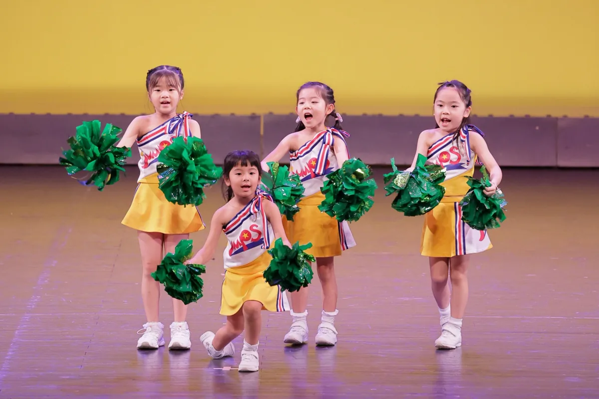 緑のポンポンを持って踊る子どもたち
