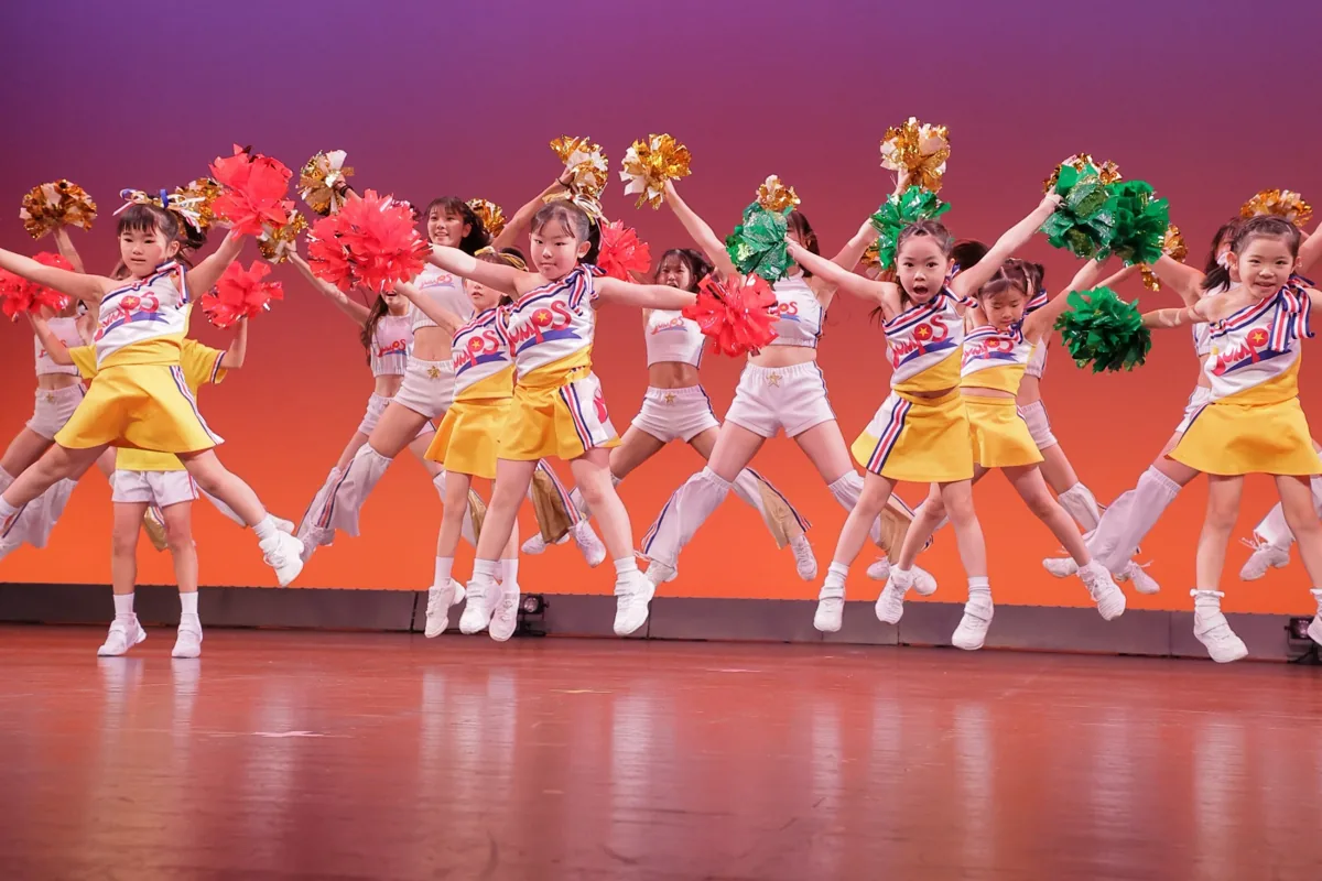 色とりどりのポンポンとともにジャンプする出演者